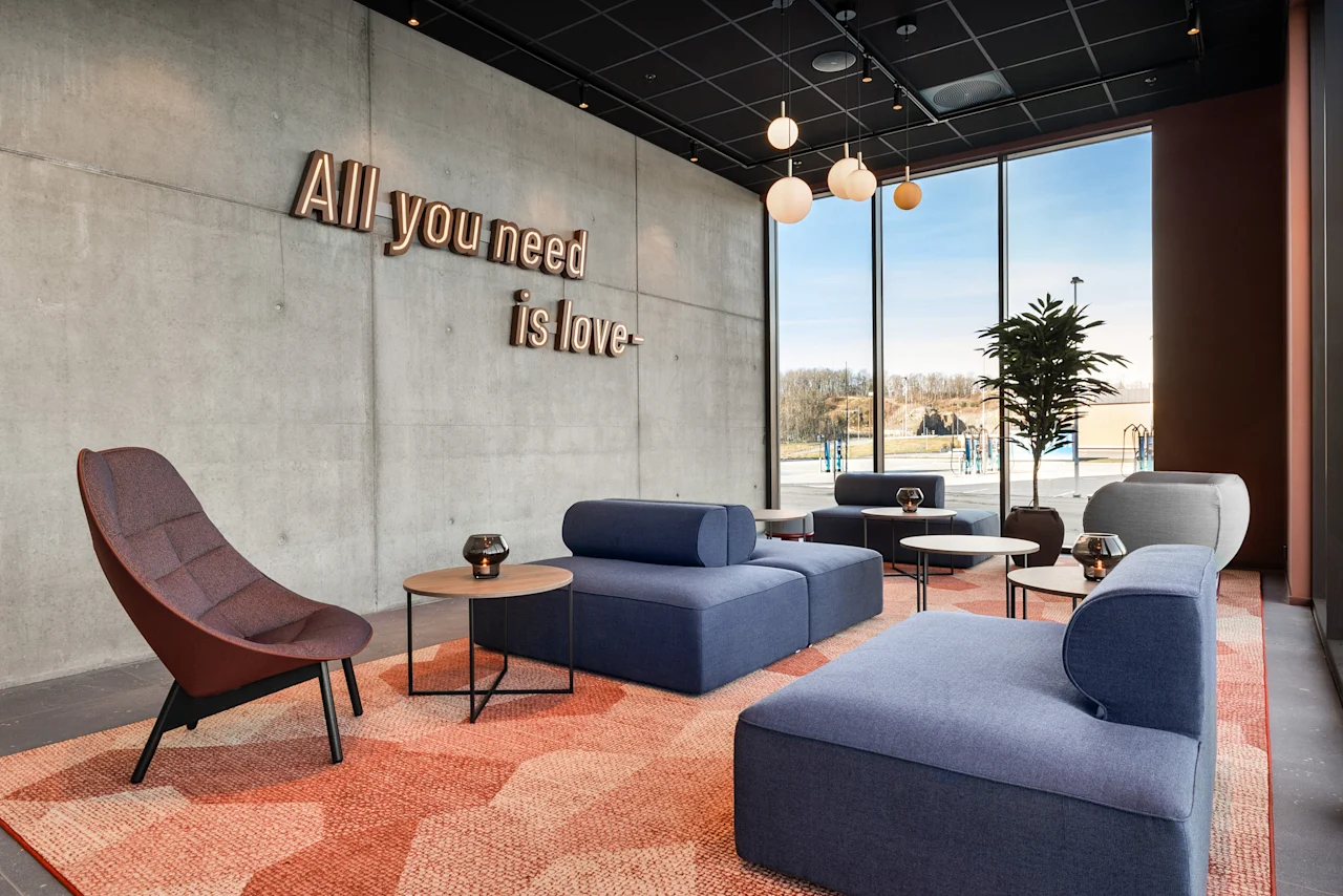 Et moderne og innbydende loungeområde med blå sofaer, mønstret teppe og betongvegg med teksten 'All you need is love'.