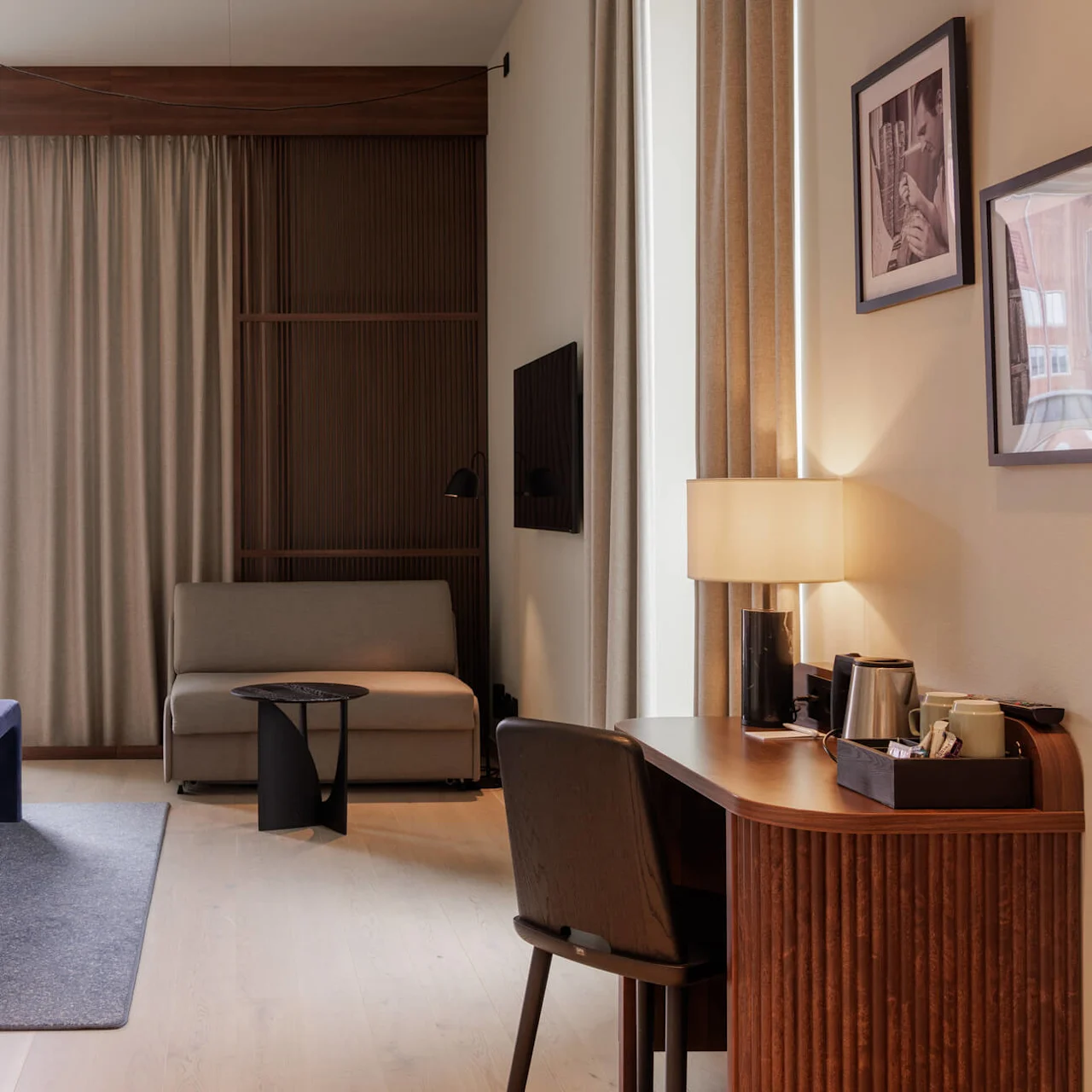 A modern hotel room with a neatly made bed, a sitting area, and a window providing natural light.