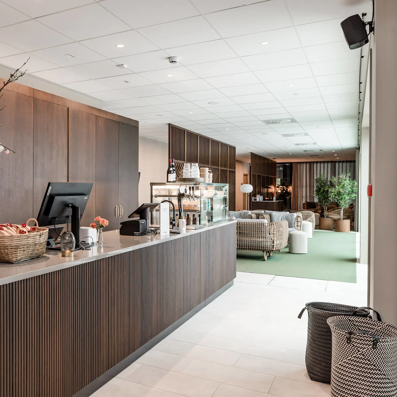 Reception med en vase blomster og kurve, beliggende i en elegant lobby med moderne indretning og rottingmøbler i baggrunden.