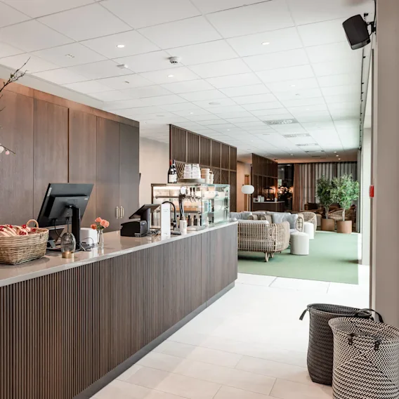 Reception desk with a vase of flowers and baskets, situated in an elegant lobby featuring modern decor and rattan furniture in the background.