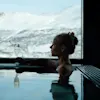 En person slapper av i et basseng, holder et champagneglass, med snødekte fjell synlige gjennom et stort vindu.