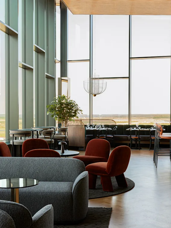 Et moderne hotellounge- og barområde med store vinduer, komfortable sitteplasser og utsikt over naturen.