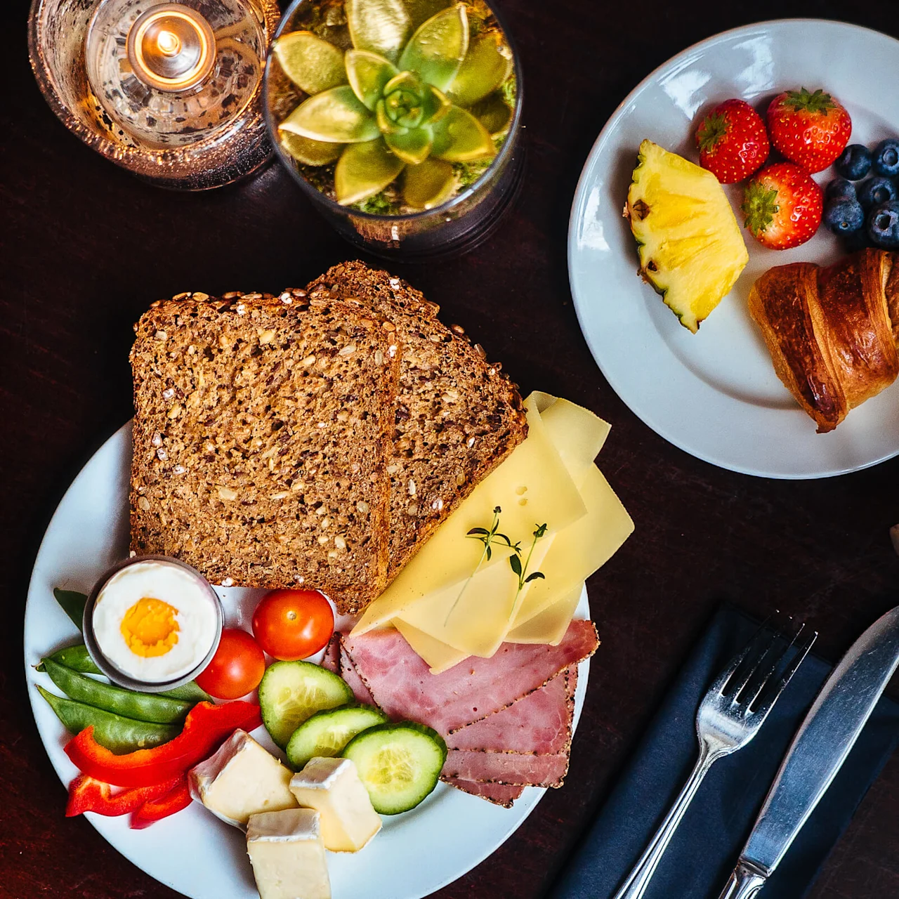 Ett frukostbord med blandade varor inklusive bröd, ost, skinka, grönsaker och kokt ägg på en tallrik, jämte kaffe.