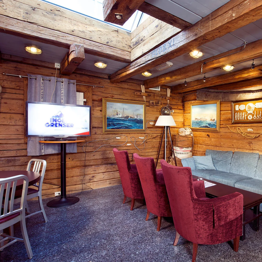 Ett mysigt maritimt inrett rum med träväggar, nautisk inredning och en TV som visar "INGEN GRENSER", inställt på restaurang eller kafé.