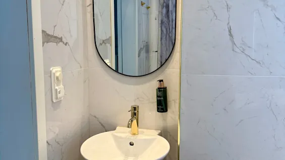 Juniorisviitti Comfort Hotel Linköping Cityssä. Moderni kylpyhuone valkoisella pesualtaalla, kultahanalla ja soikealla peilillä.