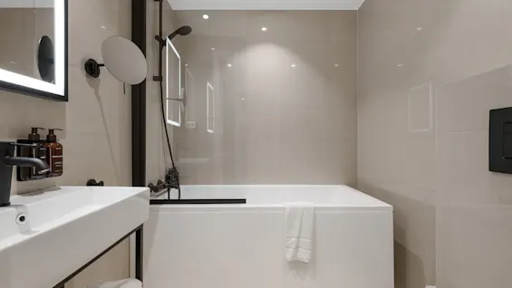 Et moderne badeværelse med hvid vask, oplyst spejl, badekar med bruser og toilet. Klar til en forfriskende oplevelse.