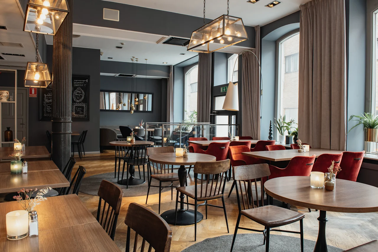 Et innbydende restaurantområde med trebord, plysj-røde stoler og myk belysning, klart for gjester å nyte et måltid.