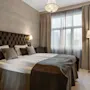 Et komfortabelt og elegant hotelværelse med en stor seng, tuftet sengegavl, lysekrone og vindue med gardiner.