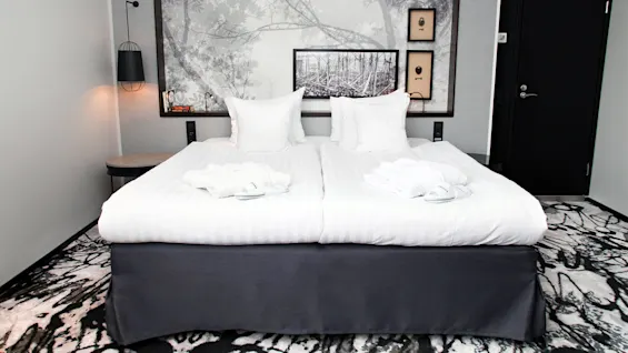 A neatly made double bed with white linens and pillows, positioned in a stylish hotel room with art on the walls.