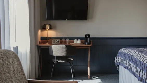 Ett soligt hotellrum med en bekväm arbetsplats med lampa, en klocka som visar 0:0 och en kaffestation.