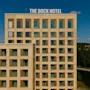 The Dock Hotel, en moderne bygning med mange vinduer, står mot en blå himmel med en grønn skogkledd bakgrunn.