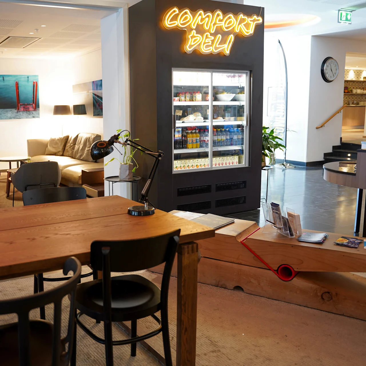 Et moderne venterom med komfortable sitteplasser, et neonskilt som leser "COMFORT DELI," og et velassortert kjøleskap, som skaper en koselig atmosfære.