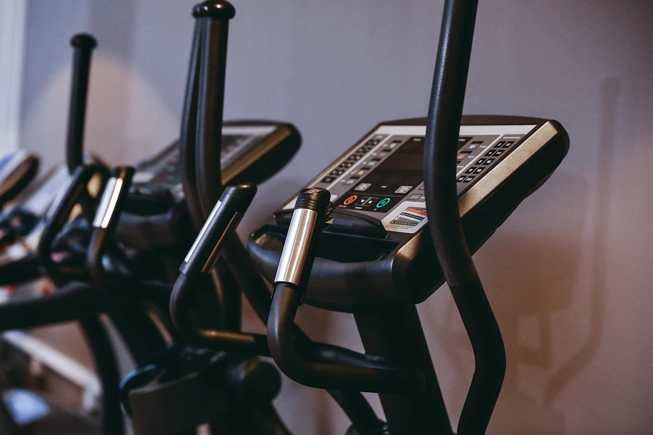 Exercise bikes with digital displays stand ready for use in a gym setting, surrounded by neutral-colored walls.