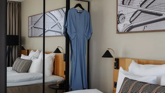 Et velutstyrt hotellrom med en komfortabel seng, et speilskap og en blå kjole klar for en utflukt.