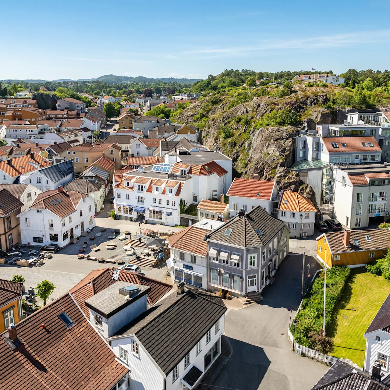 Aerial view of a European town with tightly-packed houses and buildings, nestled amongst greenery and rocky hills.