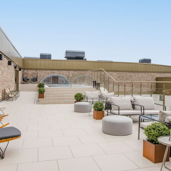 Rymlig loungedel på takterrass med moderna grå soffor, gungstolar i trä och gröna växter i krukor.