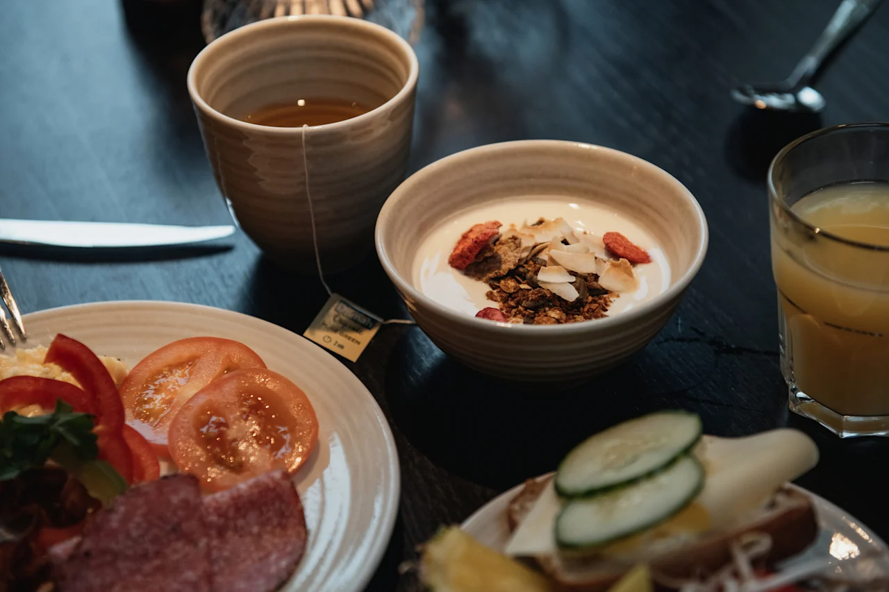 A delicious breakfast spread with tea, yogurt, fresh vegetables, cold cuts, and a sandwich at Home Hotel Kung Oscar.