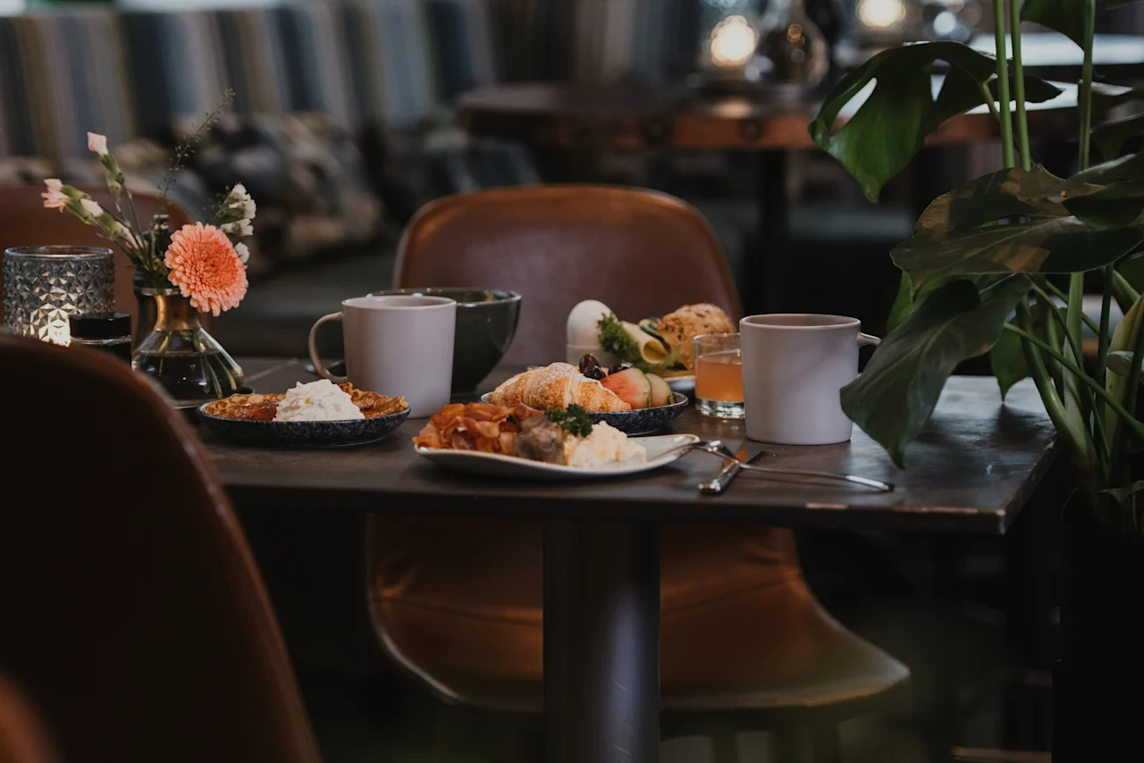 A cozy table at Home Hotel Uppsala set for breakfast with various dishes, coffee, juice, and floral decorations.