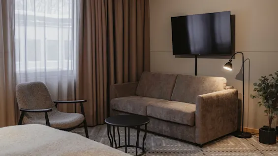 Ett mysigt hotellrum med soffa, fåtölj, TV och golvlampa, redo för avkoppling.