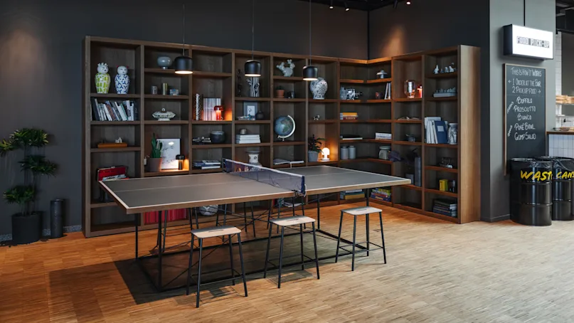 Ping pong table with stools is set in a modern room, surrounded by bookshelves filled with books and decorative items. On the wall: “FOOD PICK-UP”, “THIS IS HOW IT WORKS 1 ORDER AT THE BAR 2 PICKUP FOOD BUFALO, PROSCIUTTO, BIANCO, POKE BOWL, GUMP SALAD".