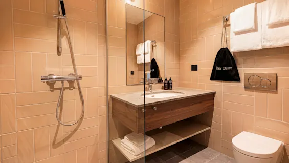 A modern bathroom at Quality Hotel The Book with a shower, sink, mirror, and toilet. A hair dryer bag hangs on the wall.