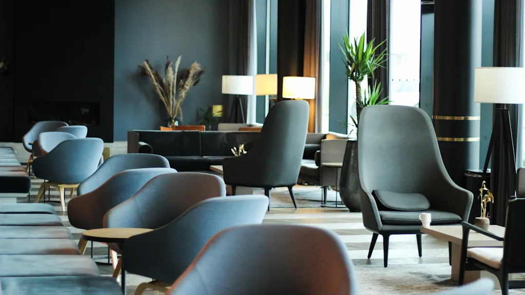 Lyxiga loungestolar står tysta i en modern hotellobby, omgivna av samtida inredning, krukväxter och mjuk belysning, vilket skapar en inbjudande och lugn atmosfär.