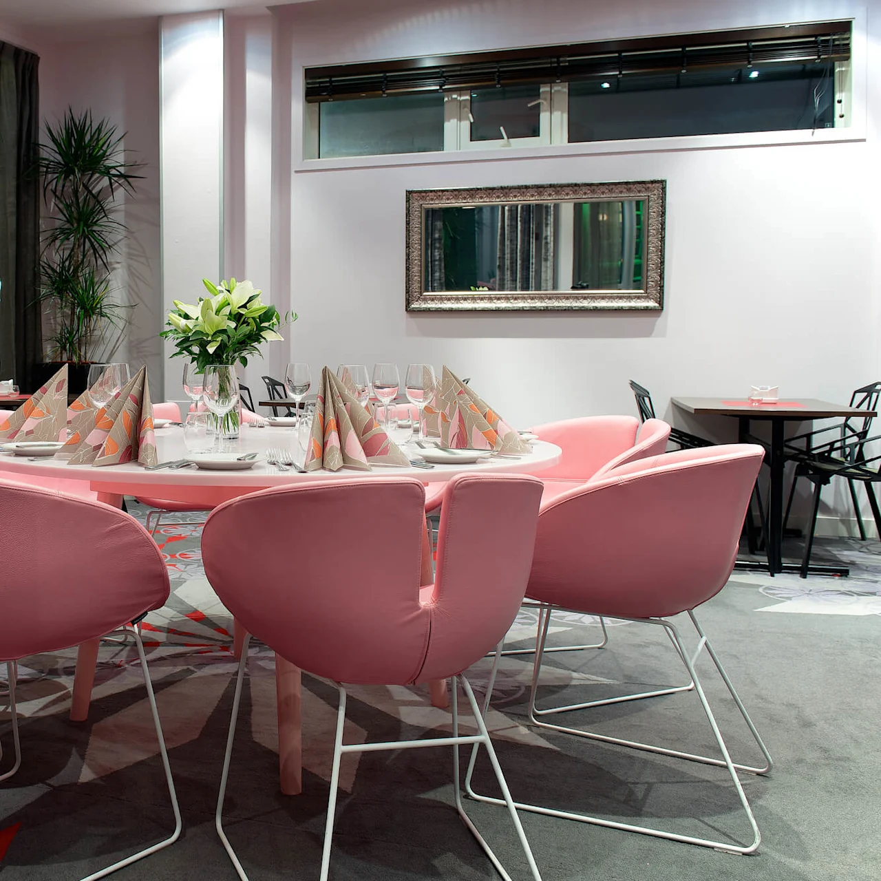 A modern dining area with a set table and pink chairs, inside a room with large windows and ambient lighting.