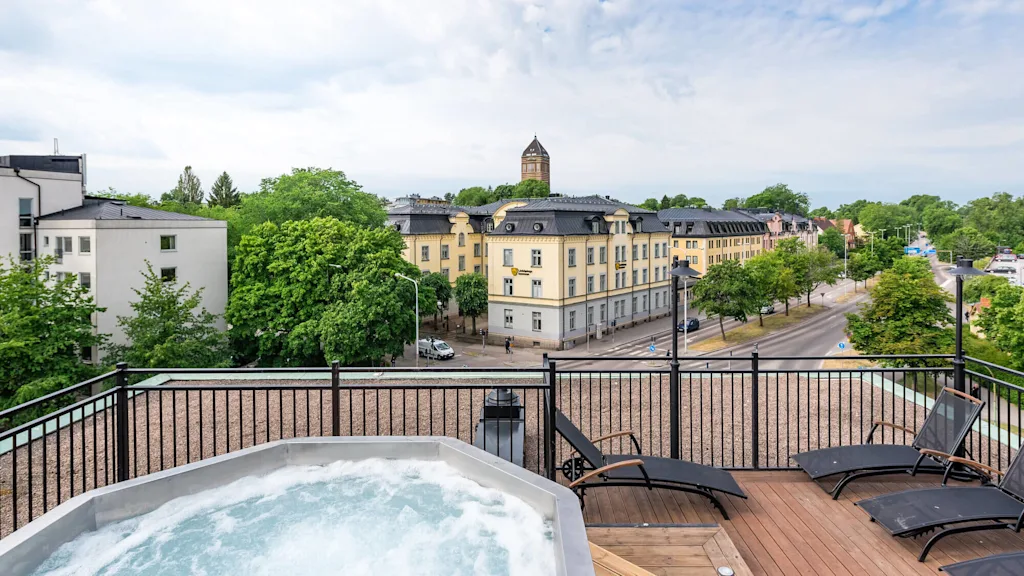 A rooftop jacuzzi with city view, surrounded by loungers on a wooden deck, under a cloudy sky.