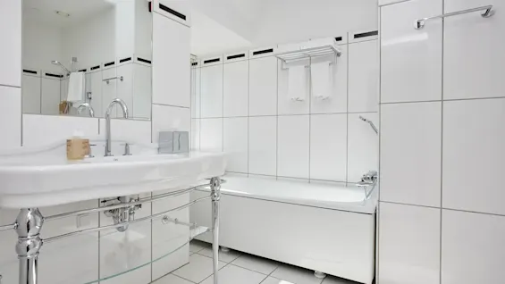 Et lyst, moderne badeværelse med hvide fliser, en elegant håndvask og et badekar, der tilbyder et rent og forfriskende rum.