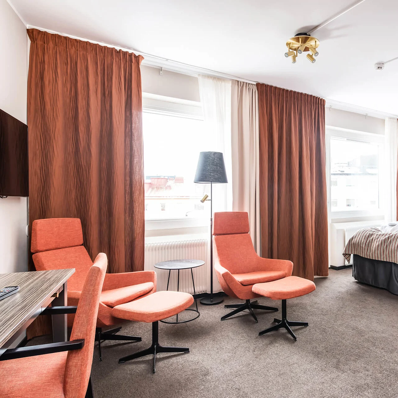 Ett välbelysat hotellrum med säng, sittplats och stora fönster.