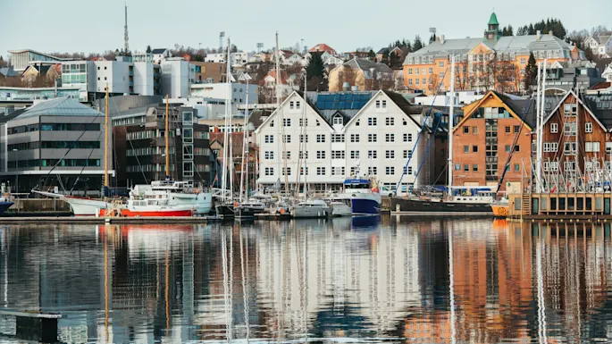 A scenic waterfront view of a city with buildings and boats reflected in the calm water.
