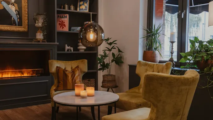 Koselig hotellounge med lenestoler, peis og dekorative gjenstander. En bok med tittelen PALM er synlig. Home Hotel Kung Oscar.