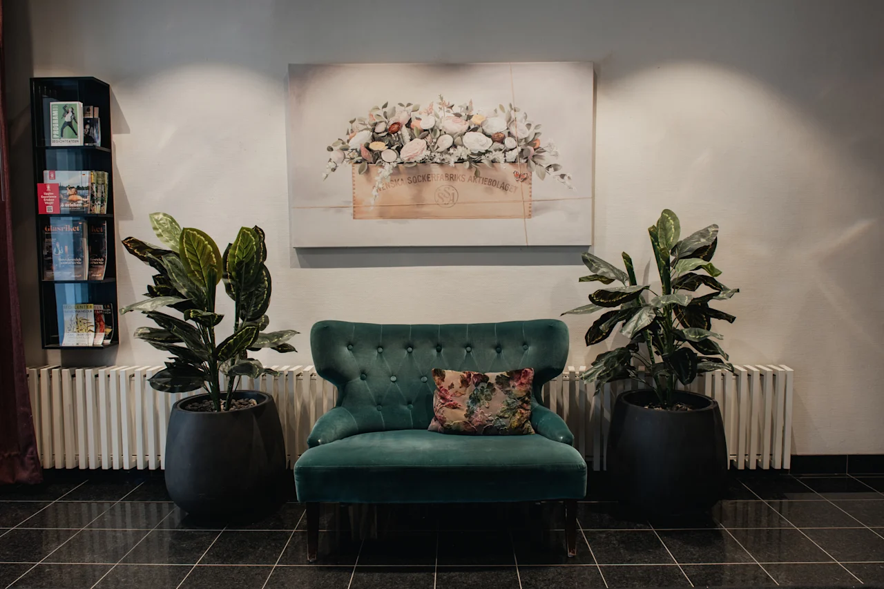 En mysig sittgrupp med en turkos fåtölj, krukväxter och en blomstermålning. Text: SOCKERBRUKS ARTIERBOLAG.