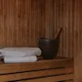 Et koselig badstuinteriør med trevegger og benker, med pent brettede hvite håndklær og en tradisjonell bøtte med øse.