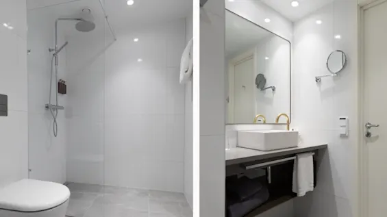 Modern bathroom with a glass shower enclosure; adjacent, a white sink with a gold faucet sits beneath a large mirror. Gray tiled floor enhances the sleek, minimalist design.
