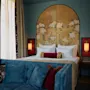 A bed with floral-patterned headboard sits in a cozy room. Two bedside lamps provide warm light. A blue sofa with decorative pillows faces the bed, creating a relaxing atmosphere.
