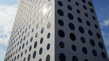 A modern high-rise building, featuring numerous circular windows, stretches upward against a blue sky with scattered clouds. Sunlight reflects off the windowed facade, creating a striking pattern.