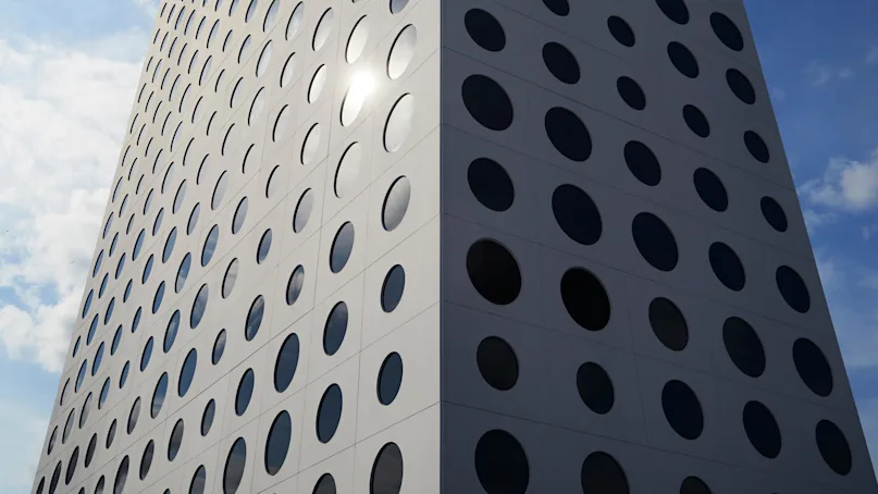 A modern high-rise building, featuring numerous circular windows, stretches upward against a blue sky with scattered clouds. Sunlight reflects off the windowed facade, creating a striking pattern.