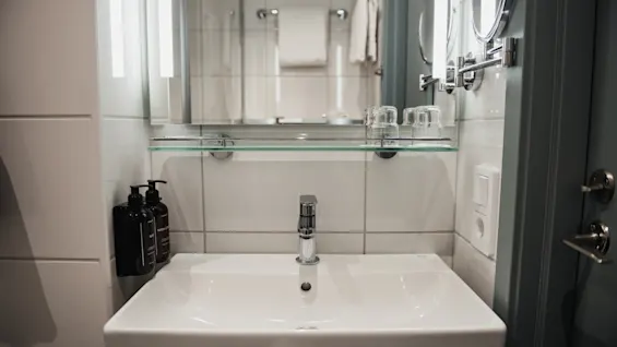 En ren och modern badrumsvask med spegel, integrerad belysning, kromkran och flaskor med kroppstvål.