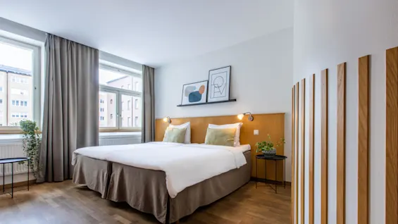 A modern bedroom with a double bed, framed art above, and wooden slats partitioning space, near a window.