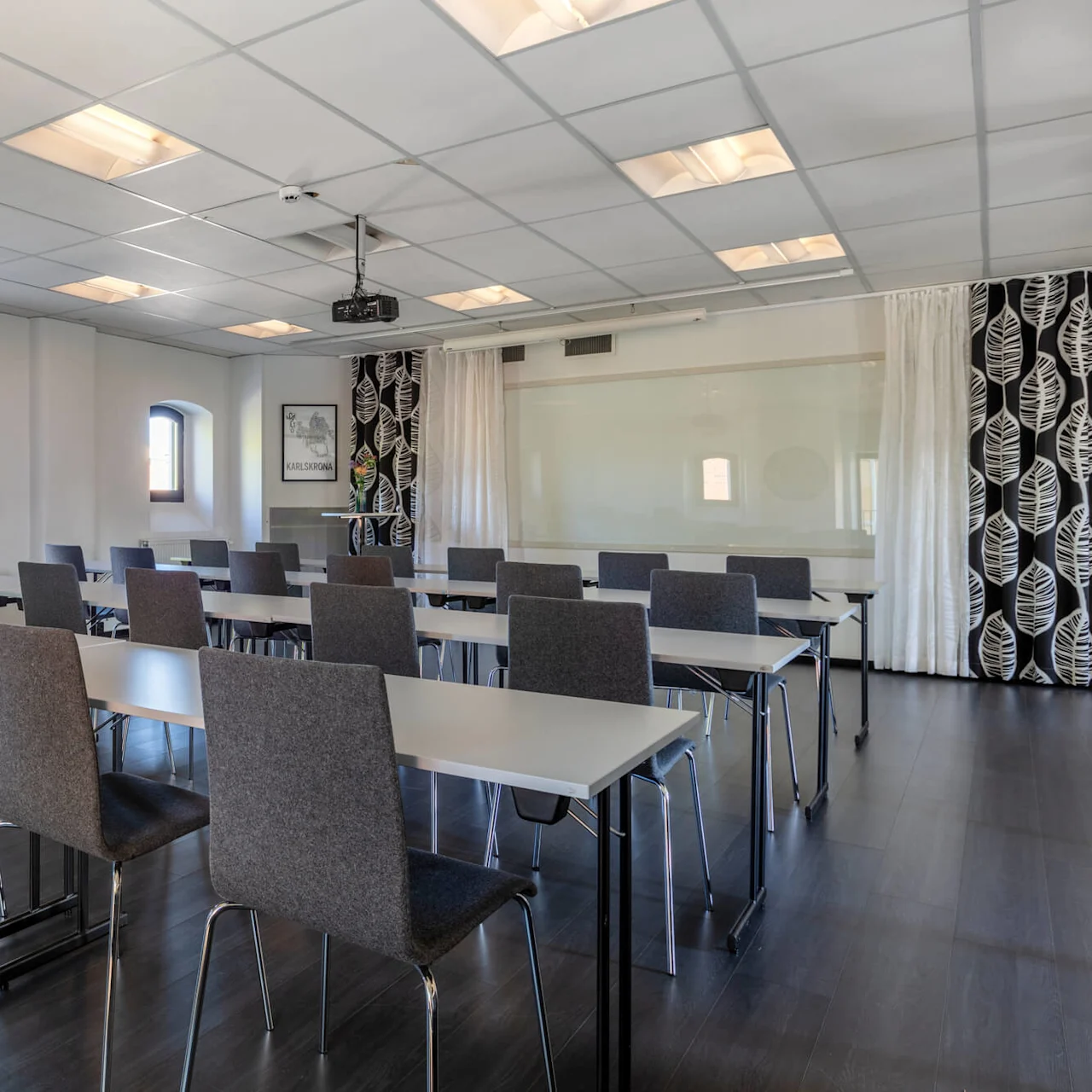 A conference room with rows of tables and chairs, projector ready, and large windows allowing natural light.