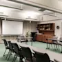 A functional meeting room at Home Hotel Grand Bodø with tables, chairs, a projector screen, and an EXIT sign. Ready for presentations.