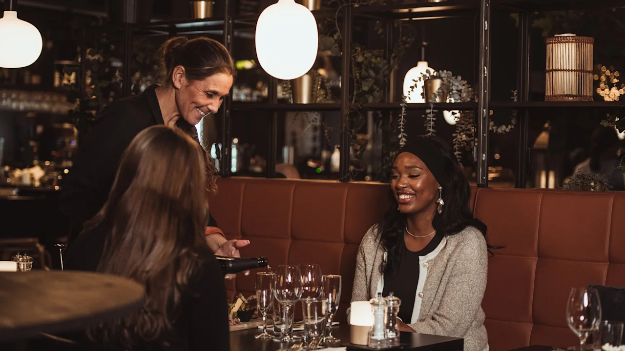 En servitris tar emot en beställning från leende gäster i en mysig restaurangmiljö.