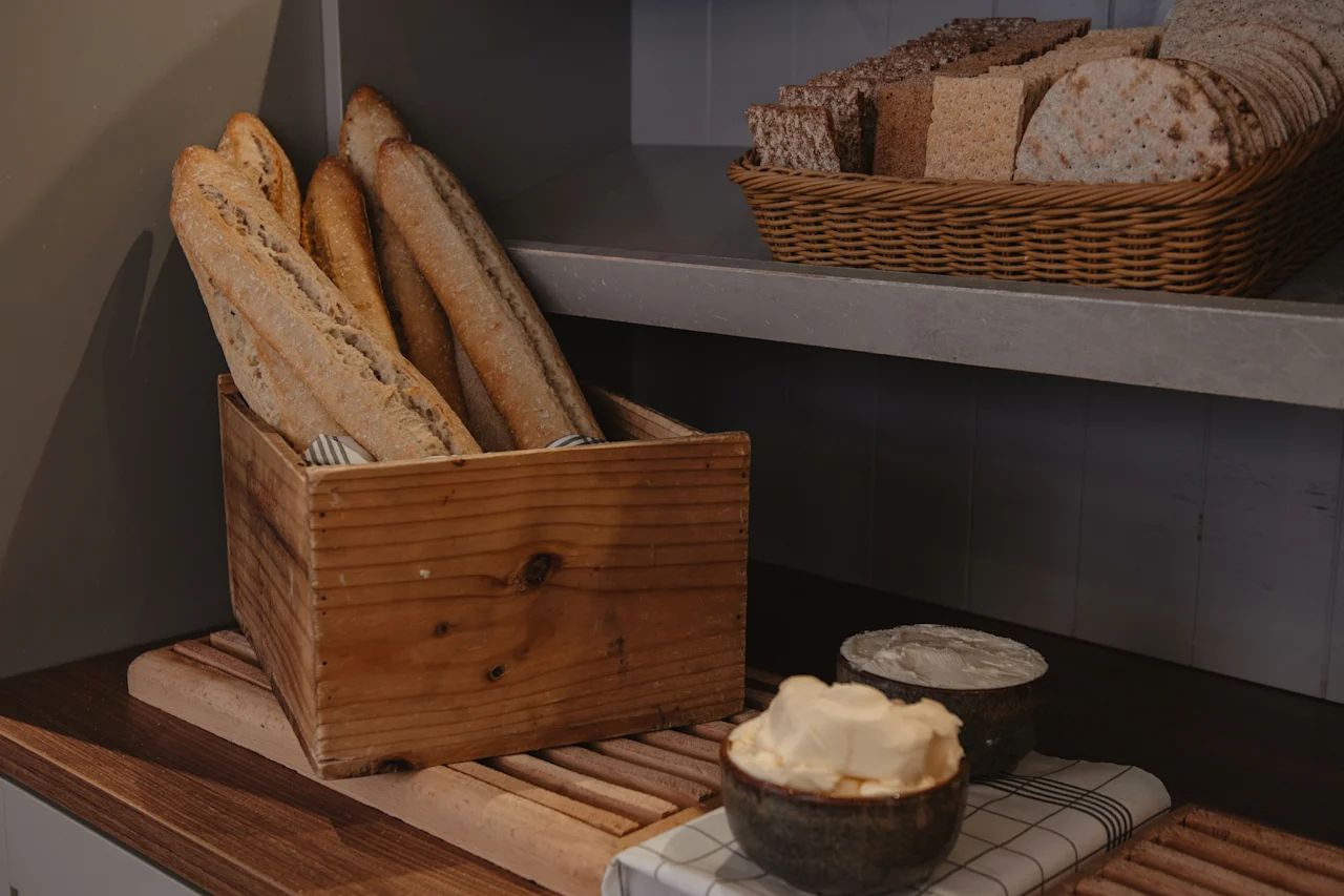 En rustikk utstilling av ferskt brød inkludert baguetter og knekkebrød, med skåler med smør og kremost.