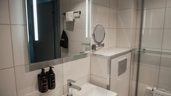 Ett modernt hotellbadrum med en ljus spegel, handfat och dusch. Bekvämligheter är prydligt arrangerade.