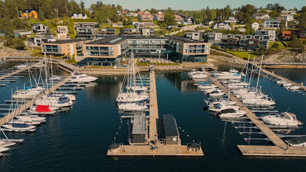 En luftfoto af en livlig marina med mange både fortøjet, mod en baggrund af moderne bygninger og huse på en bjergskråning.