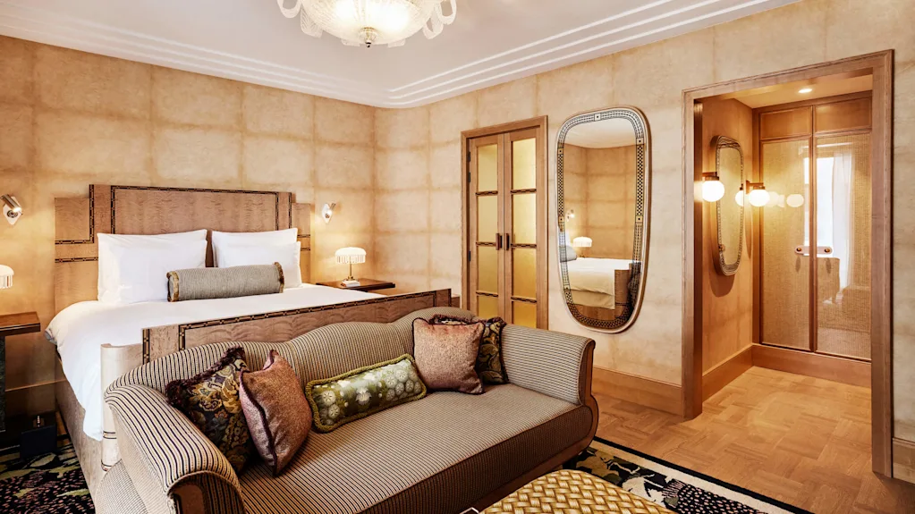 A luxurious bedroom with a large bed, striped sofa, elegant chandelier, and mirrored doors reflecting the room's interior.