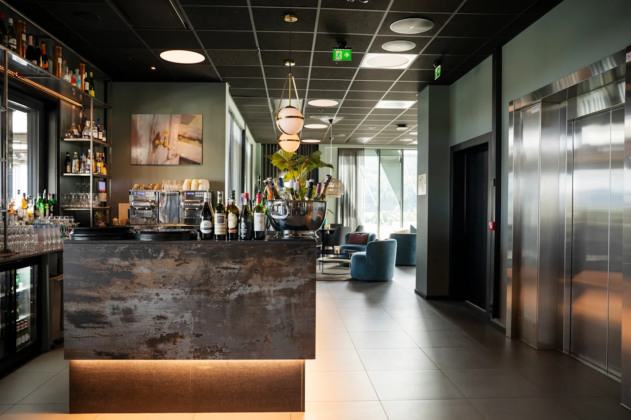 En stilig hotellobby med en velfylt bar, komfortable sittegrupper og elegante heiser.