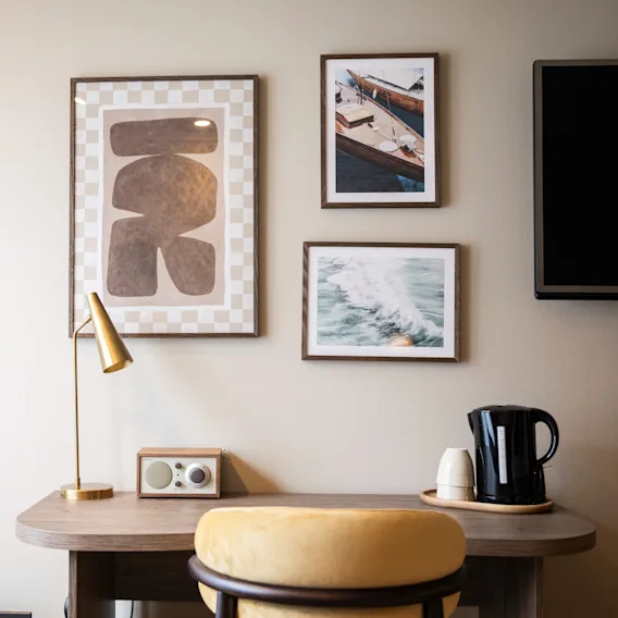 A cozy desk area in a room with framed art, a lamp, radio, and kettle, suggesting a comfortable workspace or relaxation spot.