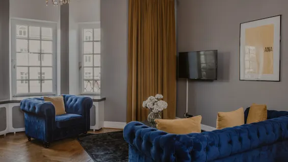 En lyxig lounge på Home Hotel Grand, Helsingborg, med blå sammetssoffor, en TV och en inramad bild med ANA.